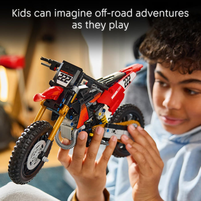 A child holds a red and black LEGO Technic off-road dirt bike with gold front fork and black tires, with a blurred indoor background and the text 'Kids can imagine off-road adventures as they play' at the top.