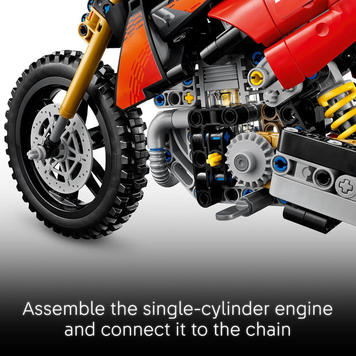 Close-up of a red and orange building block toy motorcycle engine and front wheel, with assembly instructions text at the bottom reading 'Assemble the single-cylinder engine and connect it to the chain'.