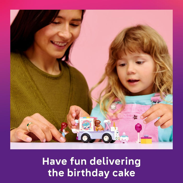 Woman and child playing with toy truck and birthday cake against a pink background