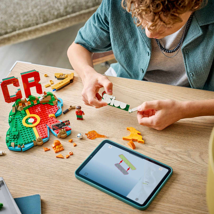 Child playing with building blocks on a table next to a tablet displaying a construction app.