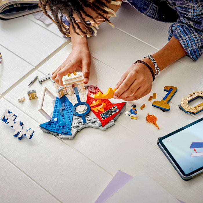 Person building a toy with colorful pieces on a table next to a tablet.
