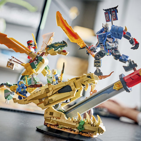 A detailed LEGO Ninjago battle scene display featuring a gold dragon on a sword with green and blue minifigures, facing a blue robot minifigure, set on a tabletop with a blurred indoor background.