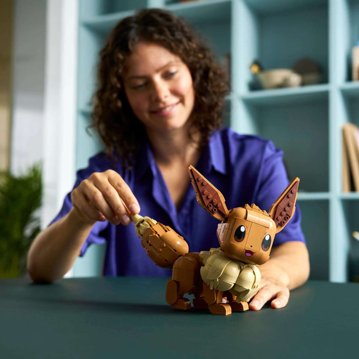 Woman holding a small brown creature figurine in a room with shelves and plants.