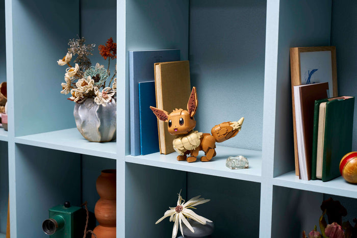 Decorative shelf with books, a small figurine, and flowers against a blue wall.