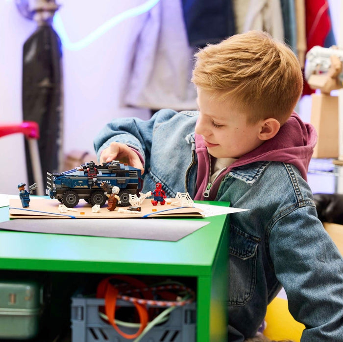 Child playing with toy cars on a desk in a room with various items