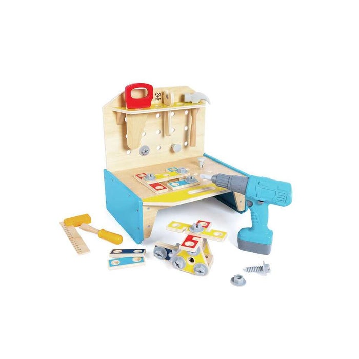 A children's wooden workbench with a variety of colorful toy tools and building pieces displayed around it, including an 'electric' drill, hammer, screwdriver, wrench, ruler, and saw.
