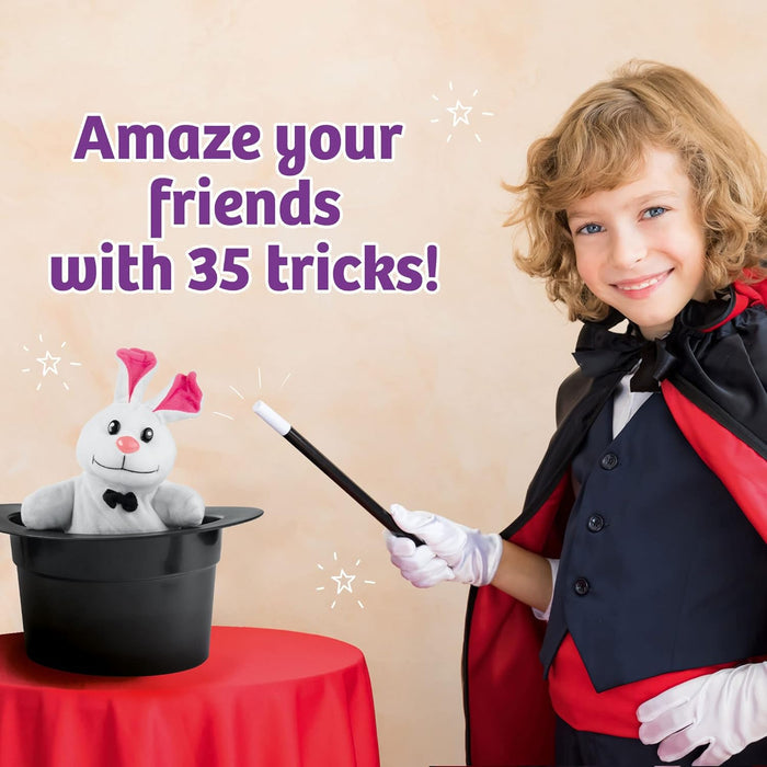 Young child dressed in a magicians cape, holding a magic wand, next to a table with a stuffed bunny popping out of the top of a top hat.