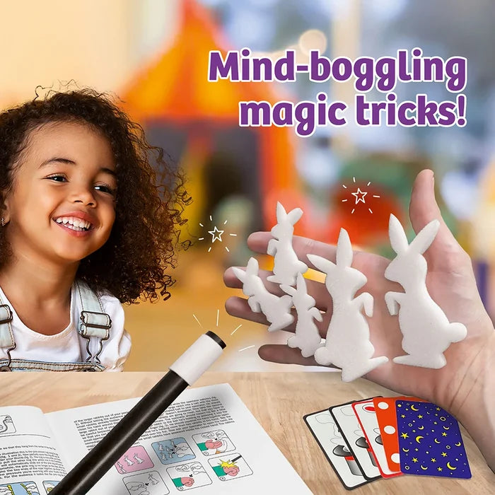 A smiling child sits at a table with a wand-like pointer and small white rabbit-shaped objects in a hand, with colorful cards and the text 'Mind-boggling magic tricks!' on a blurred playground background.