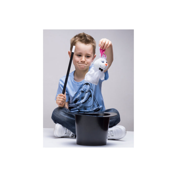 Young boy seated on the floor, holding a magic wand, pulling a rabbit out of a top hat