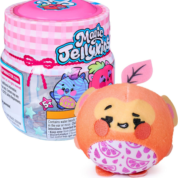 A Magic Jellykins collectible plush toy shown next to its branded plastic storage jar on a white background. The plush is orange with a yellow face, pink patterned cheeks, and a pink leaf on its head.
