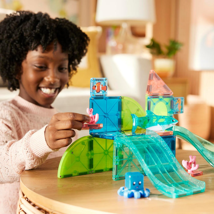 Child playing with Coral Reef Magna Tiles on a wooden table in a living room