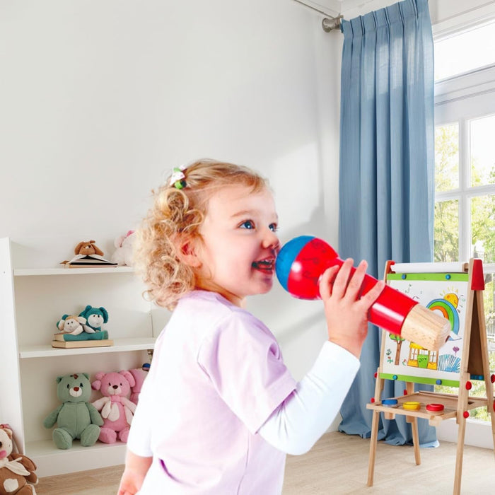 Child playing with a toy microphone in a room with toys and a window.