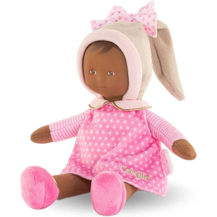 A small, soft baby doll with a pink dress, stocking cap, and shoes. The doll has a sweet, realistic vinyl face and is designed for tiny hands to hold.