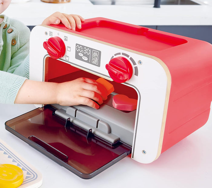 Red toy oven with digital display and knobs, being held by a child.