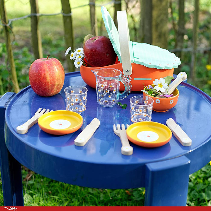Children's play picnic set with colorful dishes, basket, on a blue table outside on the grass