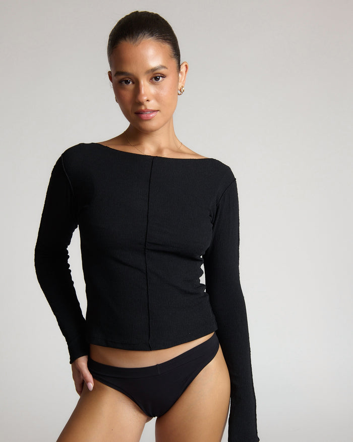 Woman wearing a black long-sleeve top and high-waisted underwear on a plain background