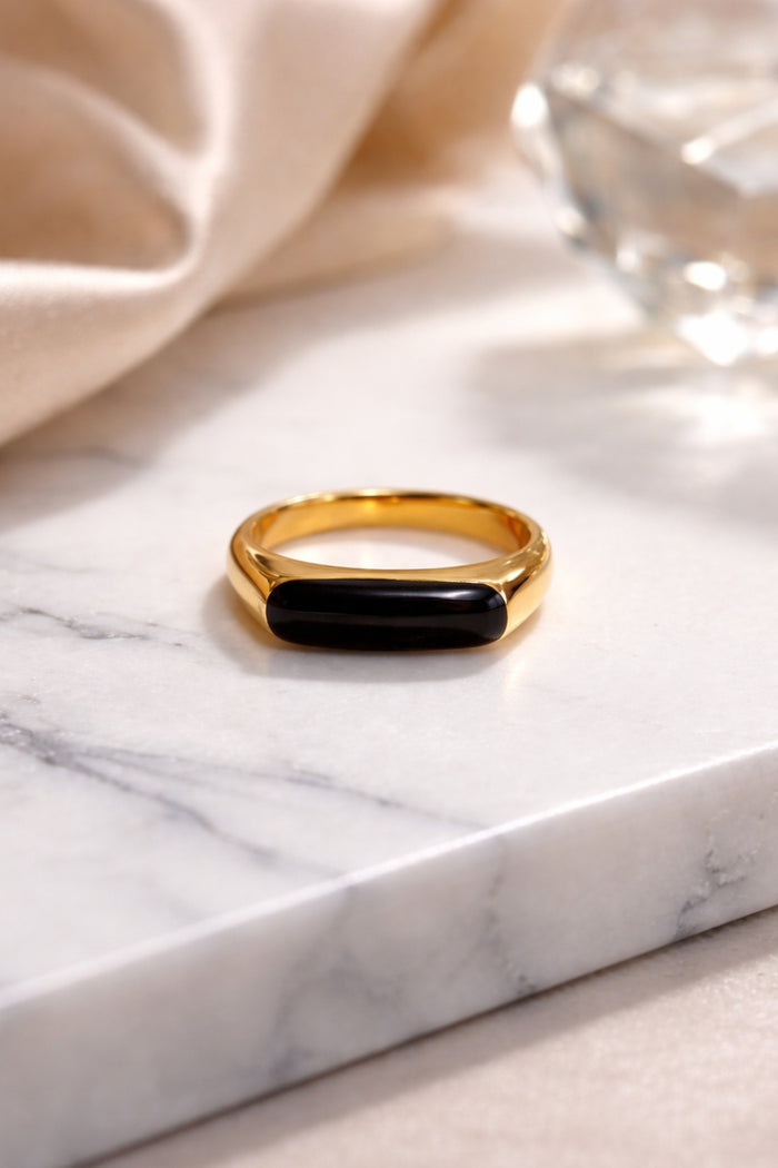 Black onyx bar gold ring on marble surface close-up, minimalist jewelry product photo with soft neutral tones and blurred background
