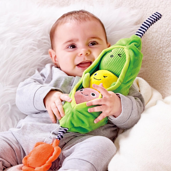 Baby holding a green plush toy with multiple faces on a white blanket