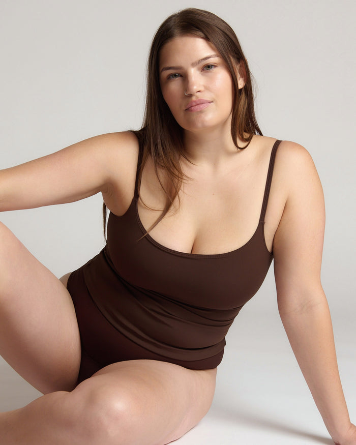 Woman wearing a brown tank top and underwear on a light gray background