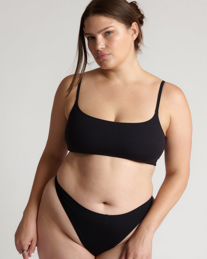 Woman wearing a black bra and underwear against a plain background