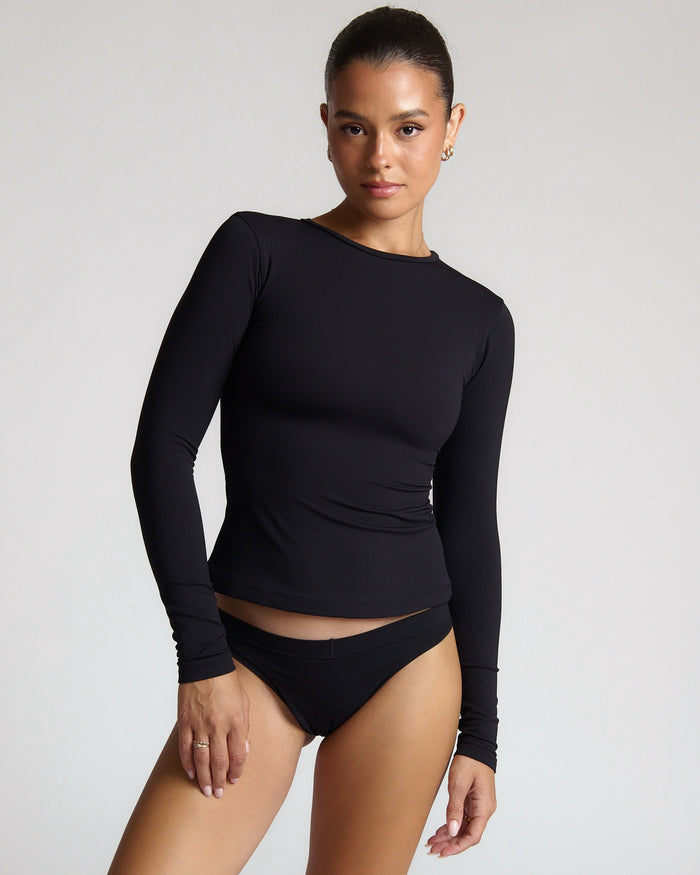 Woman wearing a black long-sleeve top and black bottom on a light gray background
