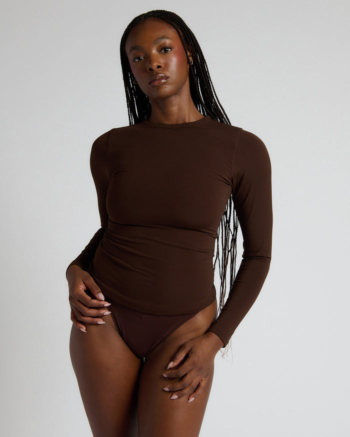 Woman wearing a brown long-sleeve bodysuit against a plain background