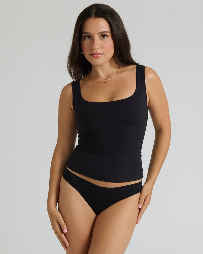 Woman wearing a black tank top and underwear on a gray background