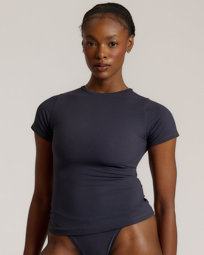 A woman modeling a myst tee and a matching thong against a plain light gray studio background.