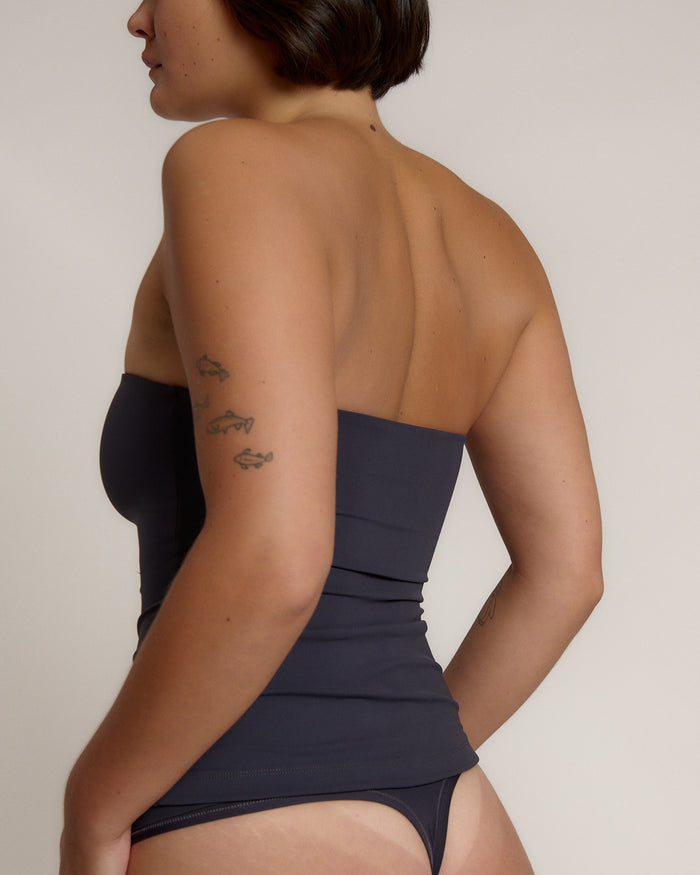 A woman modeling a myst tube top and a matching thong against a plain light gray studio background.