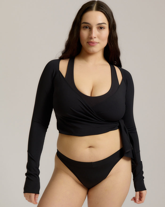 Woman wearing a black wrap top and black thong on a plain background