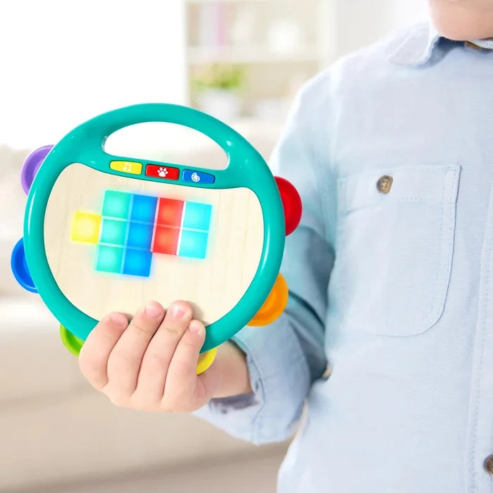 Child holding a colorful toy tambourine with buttons in a blurred indoor setting