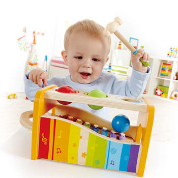 A toddler playing with a colorful wooden toy that includes a xylophone and a hammer.