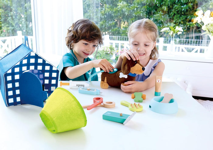 Two children playing with the Puppy Care Clinic Vet Set at a table in a bright room with large windows.
