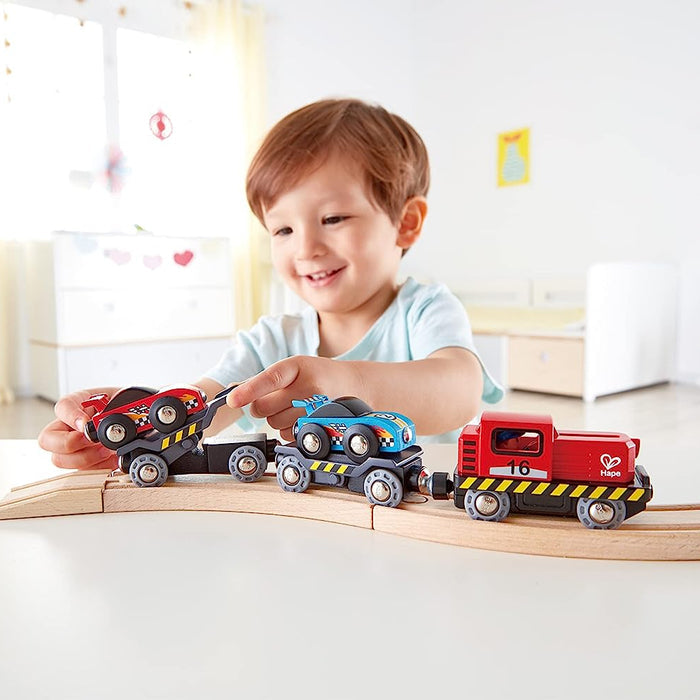 Child playing with race Car Transporter on a wooden track in a bright room.
