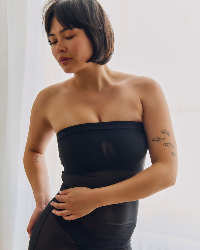Woman wearing a black sheer dress against a plain background