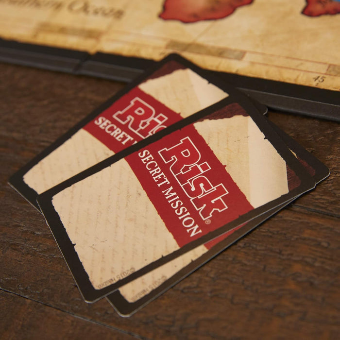 Two 'Risk' game cards on a wooden table with the game board in the background