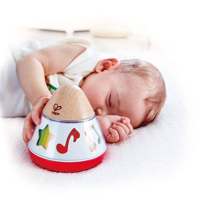 A sleeping baby lying in a crib with a colorful Rotating Music Box toy, which is designed with musical symbols and made of wood.