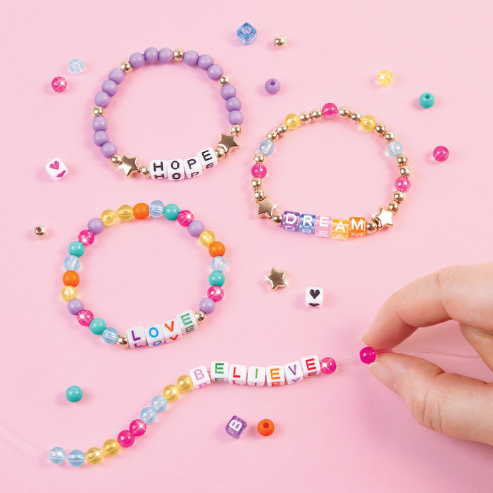 Colorful beaded bracelets with letter beads on a pink background