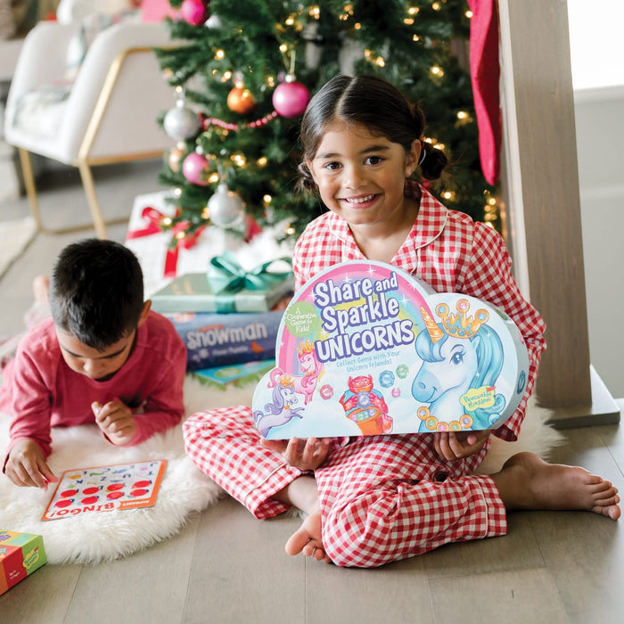 Child holding Share and Sparkle Unicorns next to a Christmas tree.