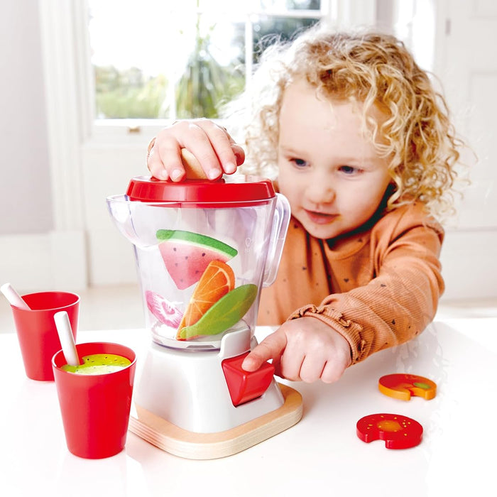 Child playing with a toy kitchen set including a red and white toy blender