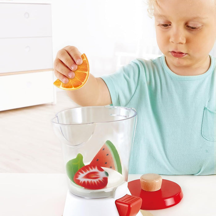Child playing with a toy blender featuring fruit designs on a white surface.