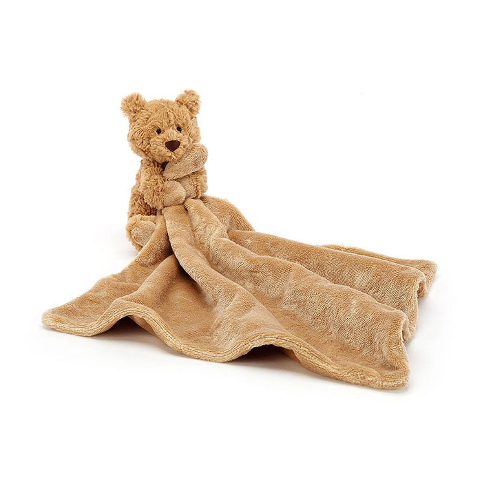 A soft plush toy resembling a black and cream puppy with perky ears, holding an un-stuffed square shaped soother, presented with a Baby Jellycat grosgrain ribbon.
