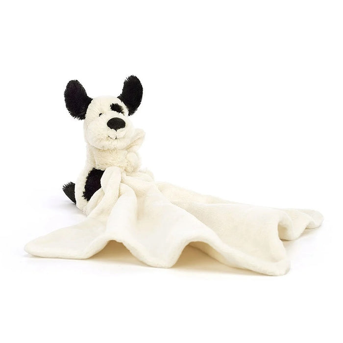 A soft plush toy resembling a black and cream puppy with perky ears, holding an un-stuffed square shaped soother, presented with a Baby Jellycat grosgrain ribbon.