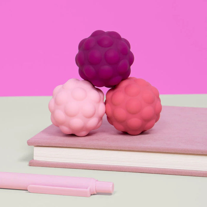 Three pink and purple textured balls on a pink notebook with a pink pen, against a pink background.