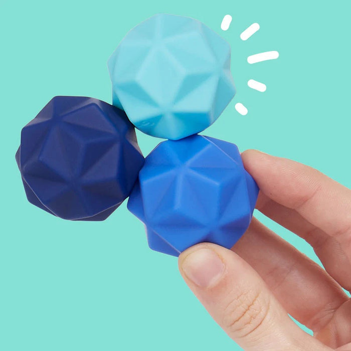 Hand holding three blue geometric-shaped objects against a teal background