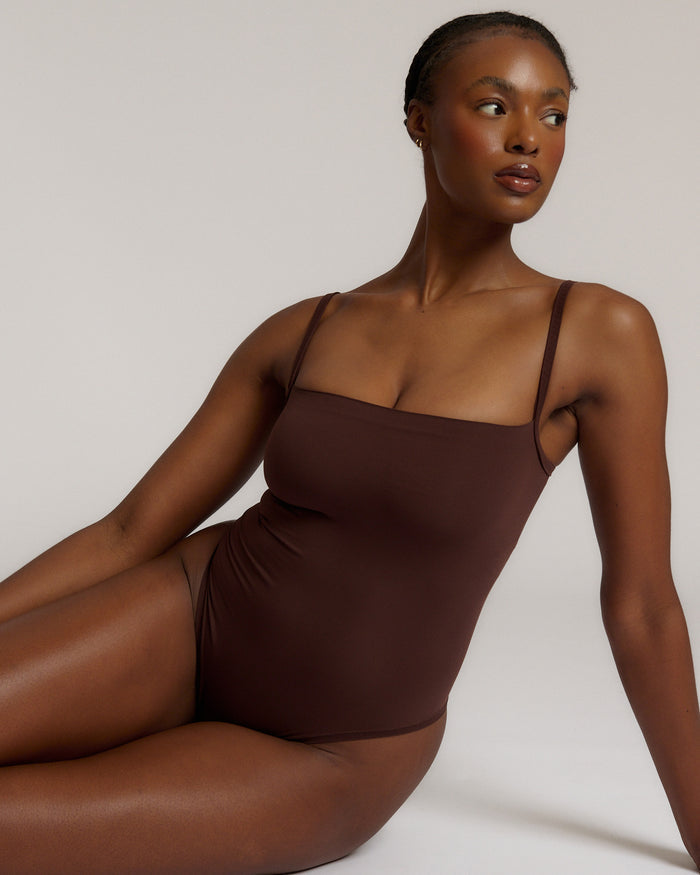 A woman wearing a brown square neck bodysuit with thin straps.