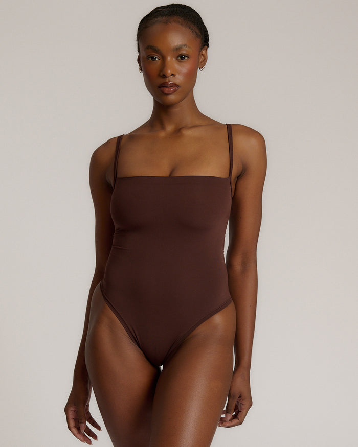 A woman wearing a brown square neck bodysuit with thin straps.