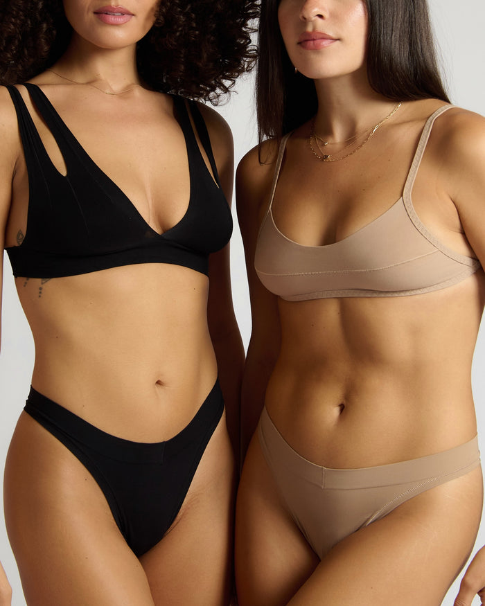 Two women wearing black and beige bras and panties against a neutral background