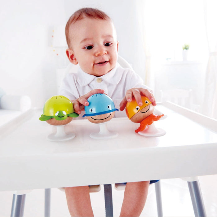 A baby sitting in a high chair playing with colorful rattle toys that have suction cups attached to them.