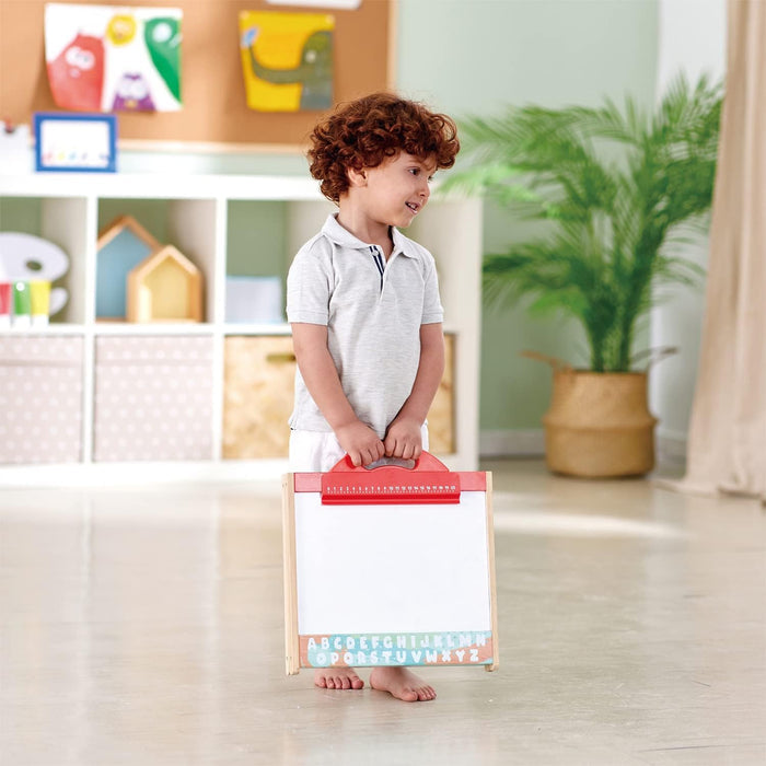 Child holding the Store and Go Easel on a wooden floor in a playroom